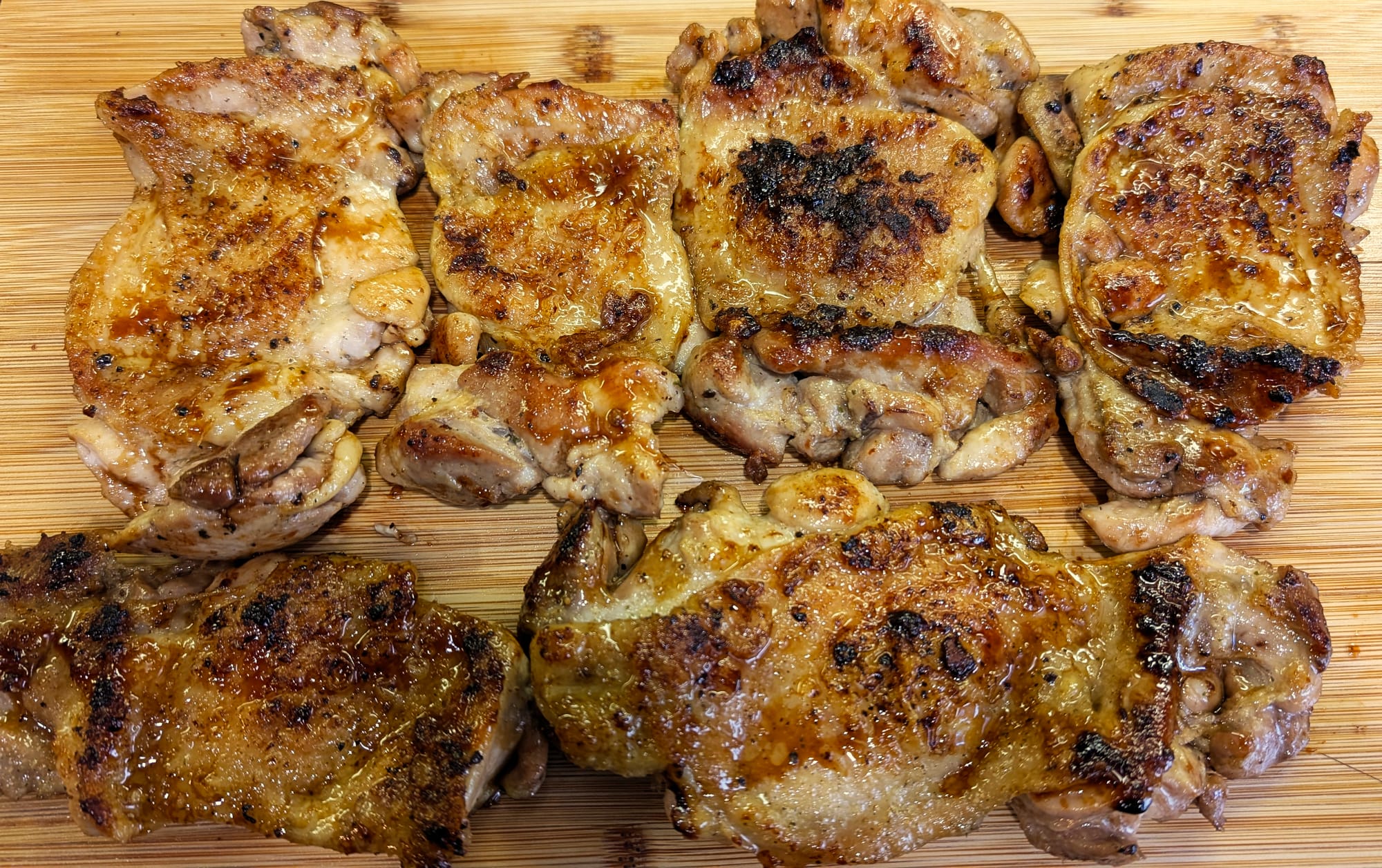 Golden pan-seared chicken thighs resting on a wooden cutting board with crispy charred edges and glossy teriyaki glaze.